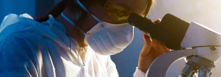 Scientist in a lab coat examines a sample under a microscope.